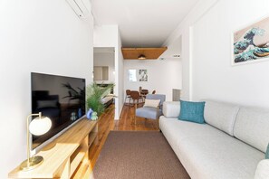 Ein modernes Wohnzimmer mit Flachbildfernseher, einer Couch, einem Essbereich und einer Holzbalkendecke.