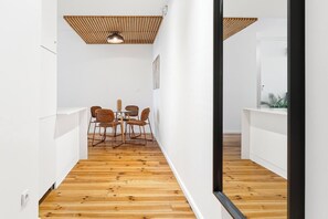 Ein schmaler Korridor mit Holzboden, weißen Wänden und einem Essbereich mit vier Stühlen und einem Tisch.