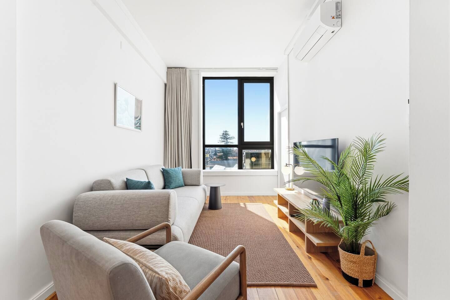 Uma sala de estar moderna com sofá, poltrona, televisão e uma grande janela com vista para a cidade.