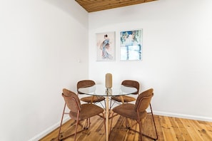 Ein Zimmer mit einem runden Glastisch, der von vier braunen Stühlen umgeben ist, weißen Wänden und Holzböden.