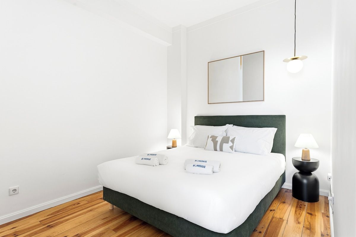 Una habitación de hotel moderna con una cama grande, dos lámparas de noche, un espejo y suelo de madera.
