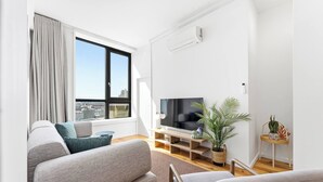 En moderne stue med stort vindue, fladskærms-tv, sofa, sofabord og et lille sidebord med en plante.