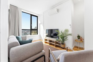 Ein modernes Wohnzimmer mit großem Fenster, einem Flachbildfernseher, einer Couch, einem Couchtisch und einem kleinen Beistelltisch mit einer Pflanze.