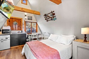 A cozy, sloped-roof bedroom with a bed, bedside lamp, and a view of a dining area with a table and chairs. - Rustic A-Frame Cabins with Tranquil Nature Views near Garden of the Gods in Colorado Springs, Colorado (Colorado Springs)