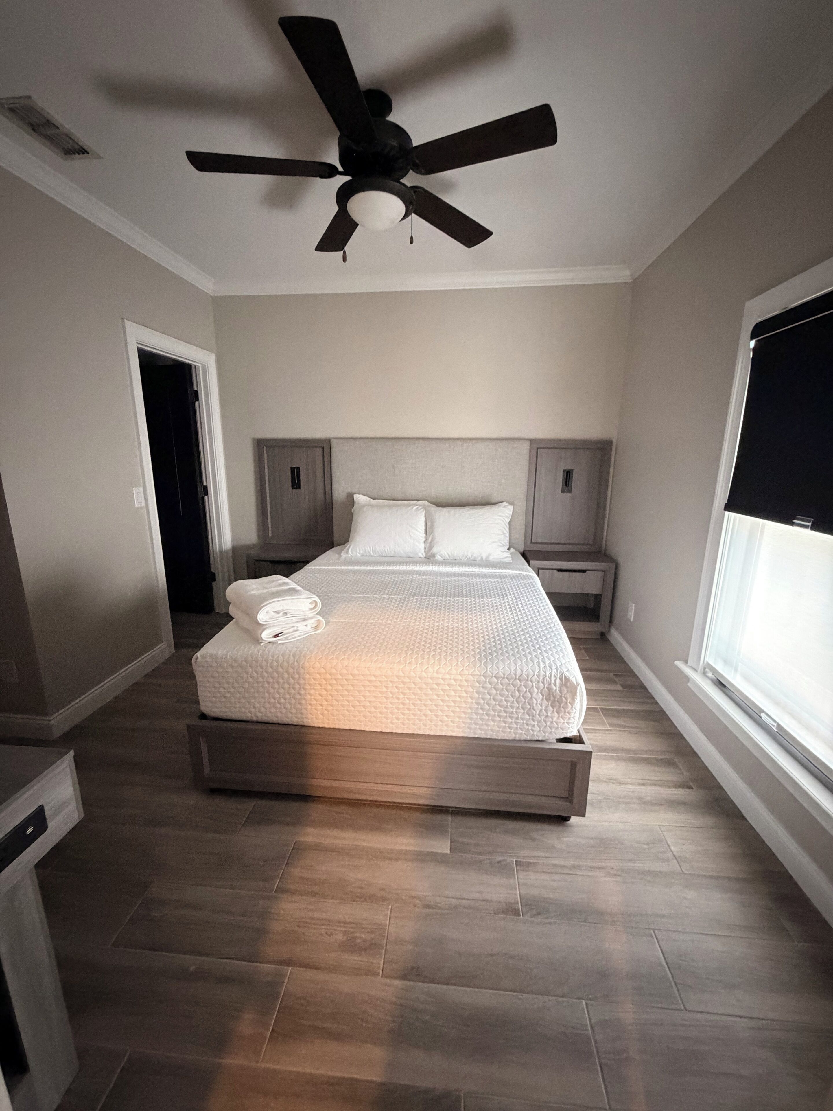 Quarto com cama, ventoinha no teto, janela e porta.