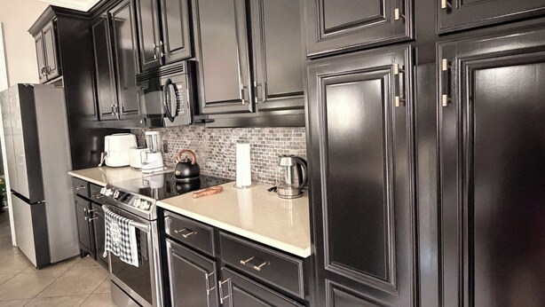 A modern kitchen with dark cabinetry, stainless steel appliances, and a tiled backsplash. - Luxury Designer Home • Disney, Universal & Downtown (Winter Park)