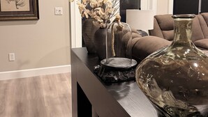 A modern living room with a dark wooden bench, a large vase with branches, a framed botanical print, and a sofa. - Luxury Designer Home • Disney, Universal & Downtown (Winter Park)