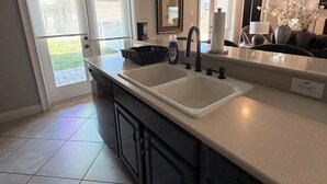 A modern kitchen with a double sink, dark cabinetry, and a large window. - Luxury Designer Home • Disney, Universal & Downtown (Winter Park)