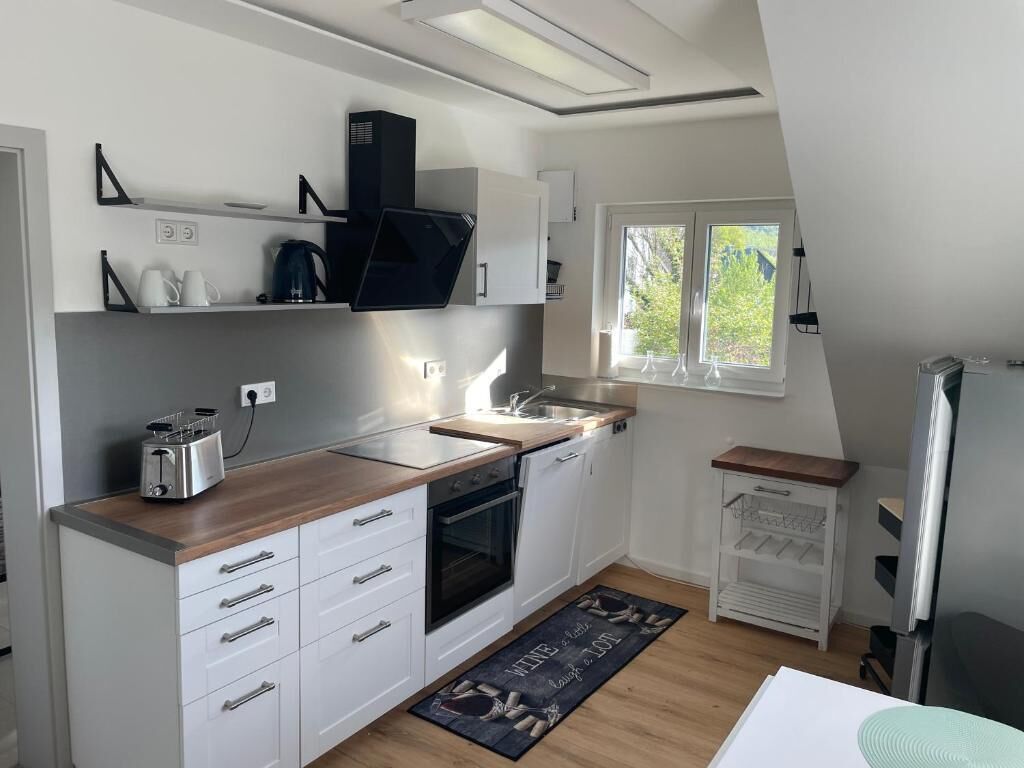 Une cuisine moderne avec des armoires blanches, un plan de travail en bois, un four encastré, une machine à café et une fenêtre donnant sur un paysage verdoyant.