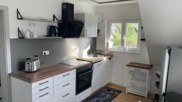 Une cuisine moderne avec des armoires blanches, un plan de travail en bois, un four encastré, une machine à café et une fenêtre donnant sur un paysage verdoyant.