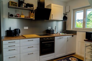 A compact kitchen with white cabinets, a built-in oven, a coffee maker, and a window providing a view of greenery outside. - Haus am Krähenbach-Steinert | Wellness rental near Lake Sorpe with sauna & WiFi (Sundern (Sauerland))