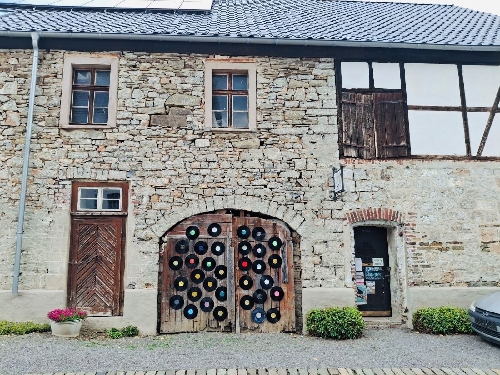 Un bâtiment en pierre avec deux portes en bois, une petite fenêtre et une enseigne.