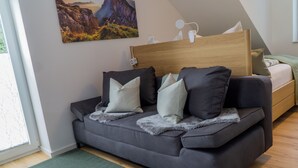 A modern bedroom with a grey sofa, a wooden headboard, and a painting of a landscape.