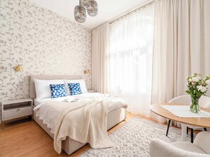 A bedroom with a bed, bedside lamps, a bedside table, a chair, a round table, and a vase with flowers. - TurnKey | Vinohrady Modern Studio with Balcony III (Prague 3)