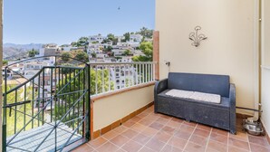 A balcony with a wicker sofa, a metal railing, and a view of a hillside town. - Vacation Home 'Bellavista Los Pinos' with Mountain Views, Private Terrace and Wi-Fi (Almuñécar)
