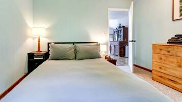 A bedroom with a bed, bedside table, lamp, dresser, and a door leading to another room.