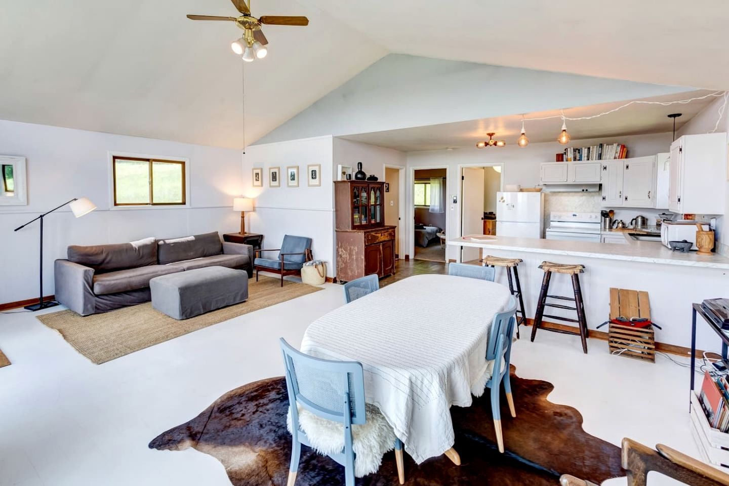 Amplia sala de estar con sofá, mesa de comedor y zona de cocina con armarios blancos.