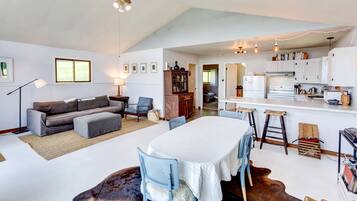 Amplia sala de estar con sofá, mesa de comedor y zona de cocina con armarios blancos.