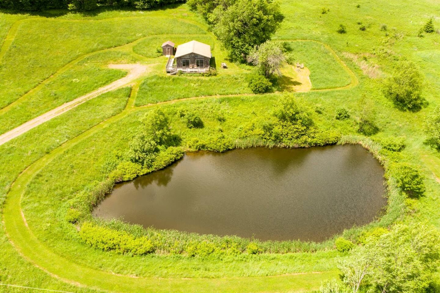Paisaje rural con un estanque, una cabaña de madera y campos circundantes.