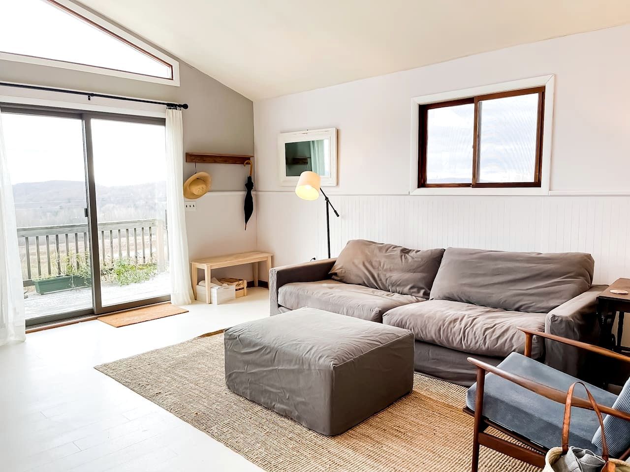 Een moderne woonkamer met een grijze bank, een bijpassend pouf, een houten bankje en een vloerlamp.
