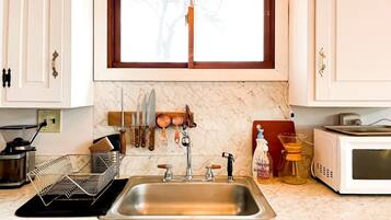 Una cocina con un lavaplatos de acero inoxidable, un microondas y una ventana sobre el lavaplatos.