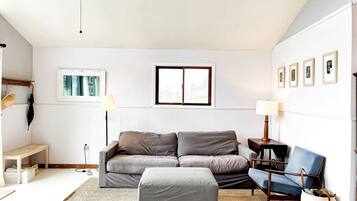 Ein modernes Wohnzimmer mit einem grauen Sofa, einem passenden Ottomanen, einem blauen Sessel, einer Stehlampe und einem kleinen Tisch.