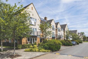 A row of modern two-story houses with balconies, a paved driveway, and a car parked on the street. - Modern 2BDR Home Near Elizabeth Line and Heathrow (Greater London)