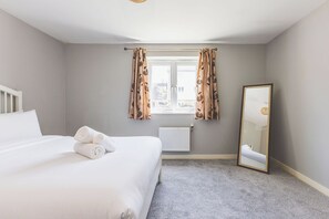 Een slaapkamer met een bed, een radiator, een raam met gordijnen en een spiegel.