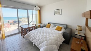 Quarto de hotel com cama, escrivaninha, cadeira, mesa, abajur e um quadro na parede.