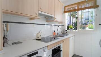 A modern kitchen with white cabinets, a built-in oven, a dishwasher, and a window with a view of greenery.