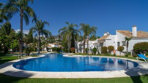 Piscina de borde curvo, rodeada de palmeras y un edificio blanco con techo de tejas.