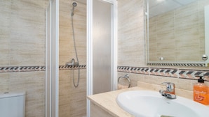 Baño con ducha, inodoro, lavabo y espejo.