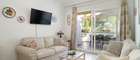 A living room with a sofa, a coffee table, a flat-screen TV, and a sliding glass door leading to an outdoor area.