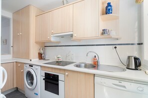Eine moderne Küche mit Holzschränken, einer Waschmaschine, einem Backofen, einem Geschirrspüler, einer Spüle und einem Wasserkocher.