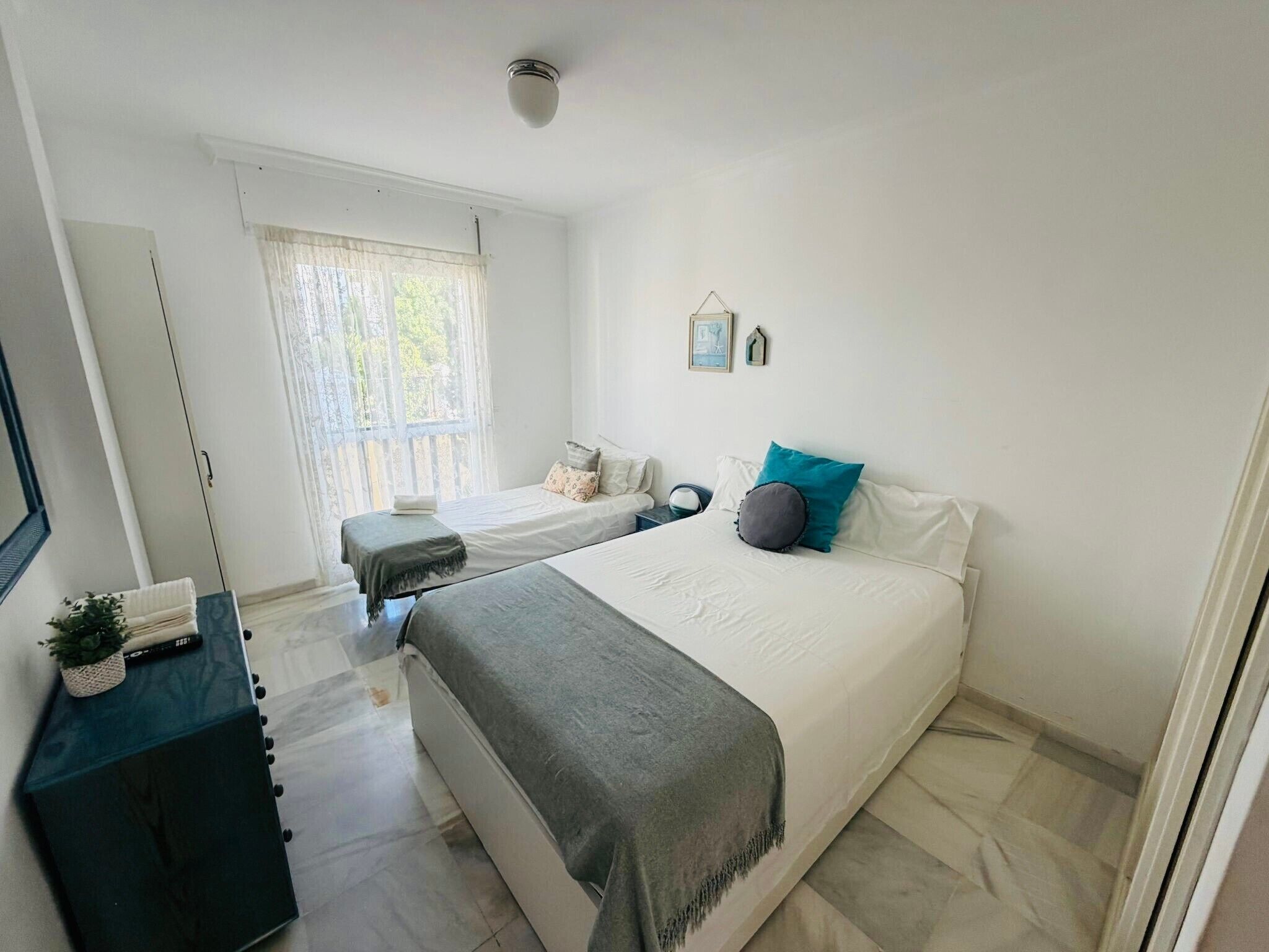 Ein Schlafzimmer mit Bett, Nachttischen, einem Schminktisch, einem Fenster mit Vorhängen und einer Deckenleuchte.