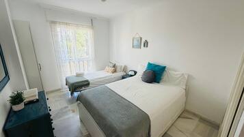 Ein Schlafzimmer mit Bett, Nachttischen, einem Schminktisch, einem Fenster mit Vorhängen und einer Deckenleuchte.