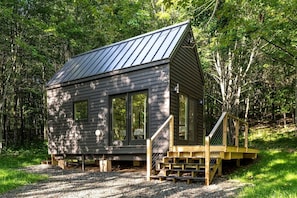 A cabin with a metal roof, large windows, and a wooden staircase leading to a deck.