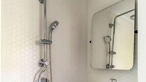 Een badkamer met een douche, wastafel en spiegel.
