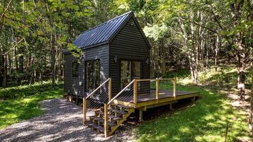 A cabin with a metal roof, wooden deck, and a staircase leading to the entrance.
