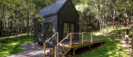 A cabin with a metal roof, wooden deck, and a staircase leading to the entrance.