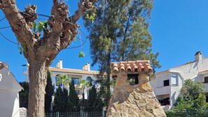 Una griglia esterna in pietra con un camino, un albero e un'area recintata con edifici sullo sfondo.
