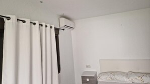 Una camera da letto con un letto, un comodino, un condizionatore e tende bianche.