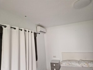 Ein Schlafzimmer mit Bett, Nachttisch, Klimaanlage und weißen Vorhängen.