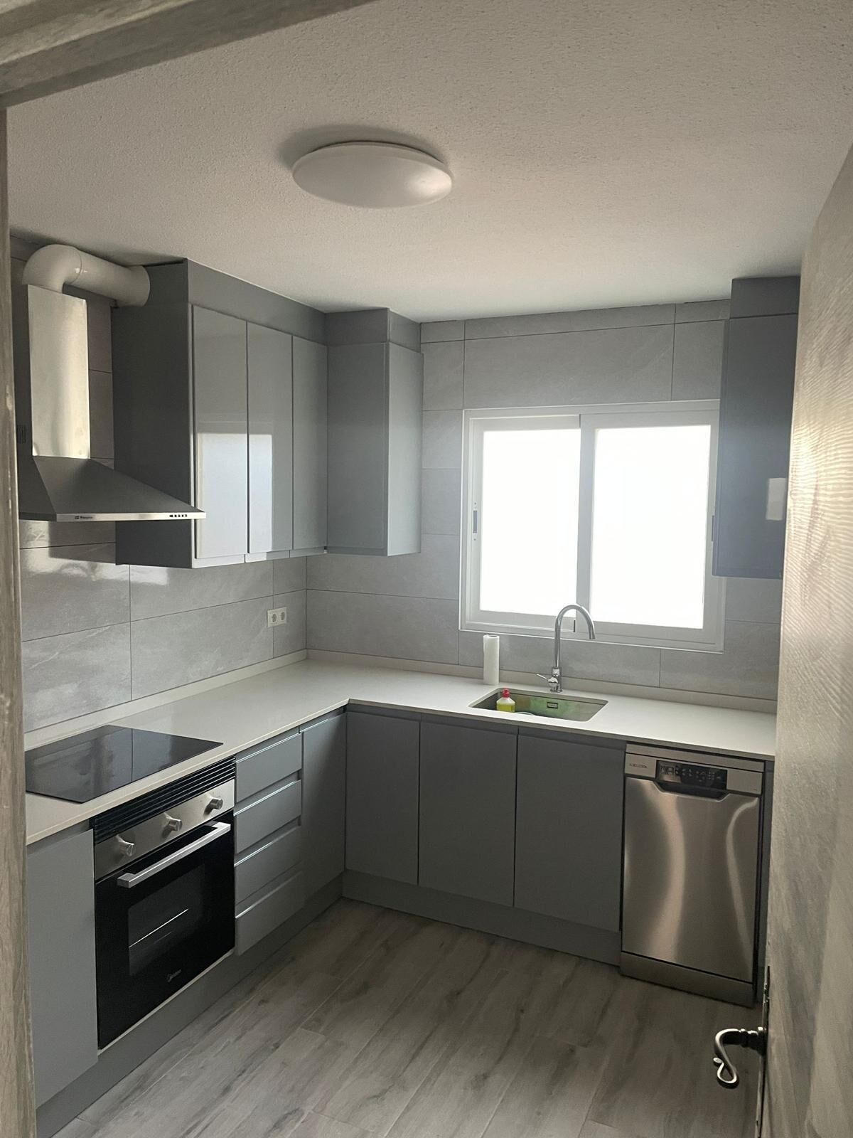 Una cucina moderna con mobili grigi, forno integrato, lavastoviglie e una finestra che fa entrare luce naturale.
