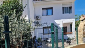 Un edificio bianco con tetto piatto, un'area esterna recintata con sedie e tavoli e un cielo blu limpido.