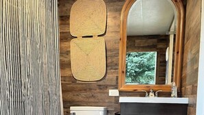Ein Badezimmer mit Toilette, einem dunklen Holzschrank, einem Spiegel und einem gestreiften Duschvorhang.