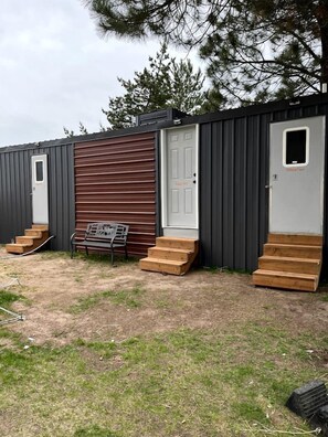 En flyttbar byggnad med en bänk, trästeg och en dörr med texten ”Willow Tent” (Pilträdstältet).