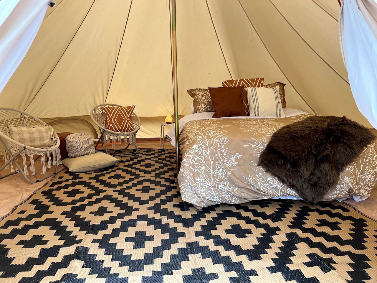 A tented room with a bed, two chairs, a patterned rug, and a fluffy pillow.