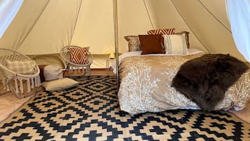 A tented room with a bed, two chairs, a patterned rug, and a fluffy pillow.
