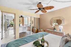 A bedroom with a bed, a ceiling fan, a mirror, and a view into another room. - Tropical Retreat, steps from Charlie Young Beach (Kihei)